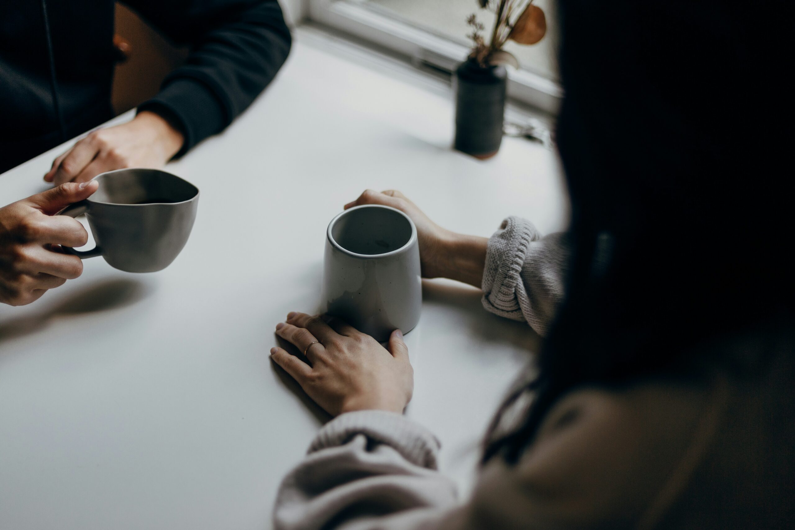 Hands of two women at a table, each holding cups of coffee in conversation